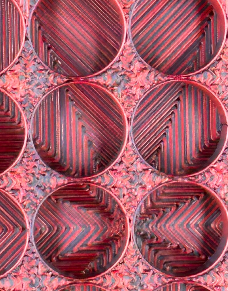 May include: Close-up of a red and black textured surface with a repeating pattern of circular indentations. The surface has a rough, almost metallic look.