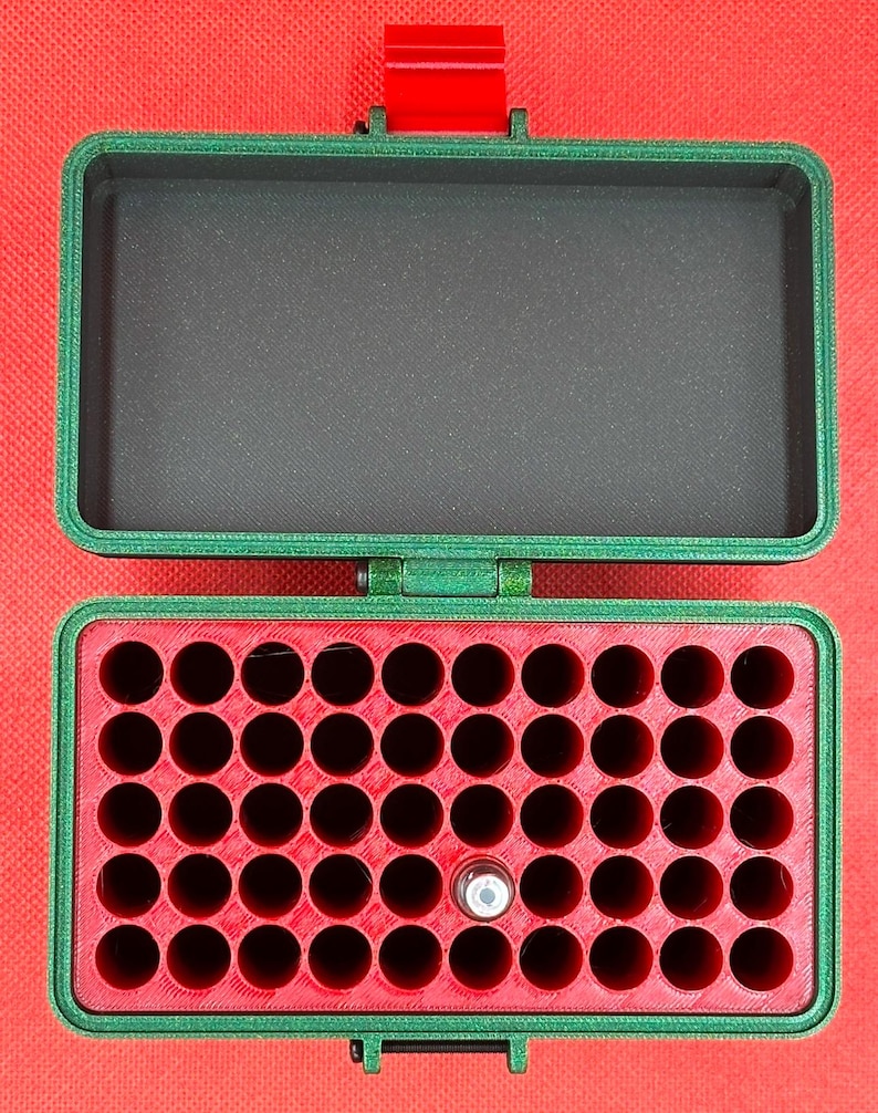 May include: A rectangular green storage case with a hinged lid and a red latch. The interior features a red insert with forty-eight circular holes for small items, and one small silver cylindrical object is placed in one of the holes.