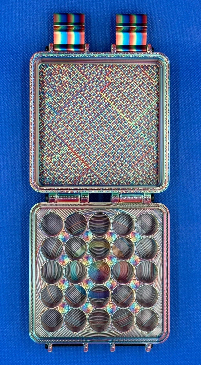May include: A square, iridescent, multi-colored storage case with a hinged lid. The interior of the lid features a textured, cross-hatched pattern, while the base contains a grid of twenty circular, concave compartments with a spiral finish.