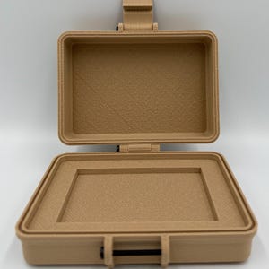 Puede incluir: Peque&ntilde;o malet&iacute;n beige abierto, con interior texturizado. De forma rectangular, tiene tapa con bisagras y cierre negro. El malet&iacute;n est&aacute; hecho de un material s&oacute;lido y parece estar vac&iacute;o.