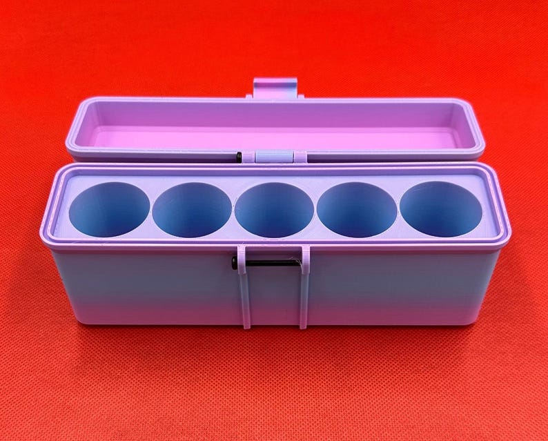 May include: A rectangular storage case with a hinged lid, featuring a gradient color scheme that transitions from light purple to blue. The interior contains five circular compartments arranged in a single row, designed for holding cylindrical items.