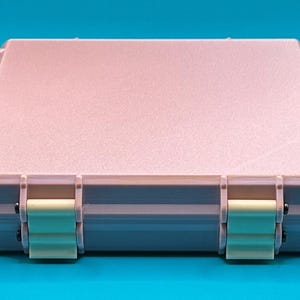May include: A light pink plastic storage case with two latches on the front. The case has a textured surface and is closed.