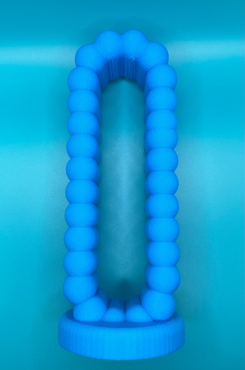 May include: A light blue 3D printed object shaped like a tall, narrow archway with a rounded top and bottom. The object is made up of a series of small, round spheres that are connected together.