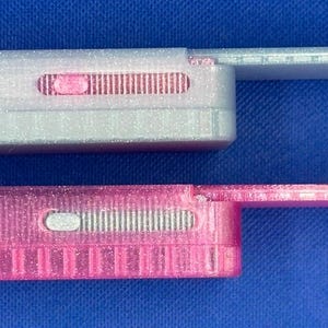 May include: Two rectangular sliding cases with a glittery finish. The top case is translucent white with a pink sliding mechanism, and the bottom case is translucent pink with a white sliding mechanism. Both feature a side-extending tab.