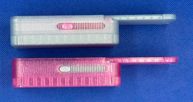 May include: Two rectangular sliding cases with a glittery finish. The top case is translucent white with a pink sliding mechanism, and the bottom case is translucent pink with a white sliding mechanism. Both feature a side-extending tab.