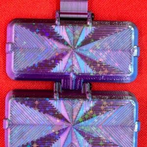 May include: A dual-section rectangular container featuring a deep purple frame and a holographic, star-patterned inlay. The surface displays a radiating geometric texture with iridescent blue and purple light reflections across the panels.