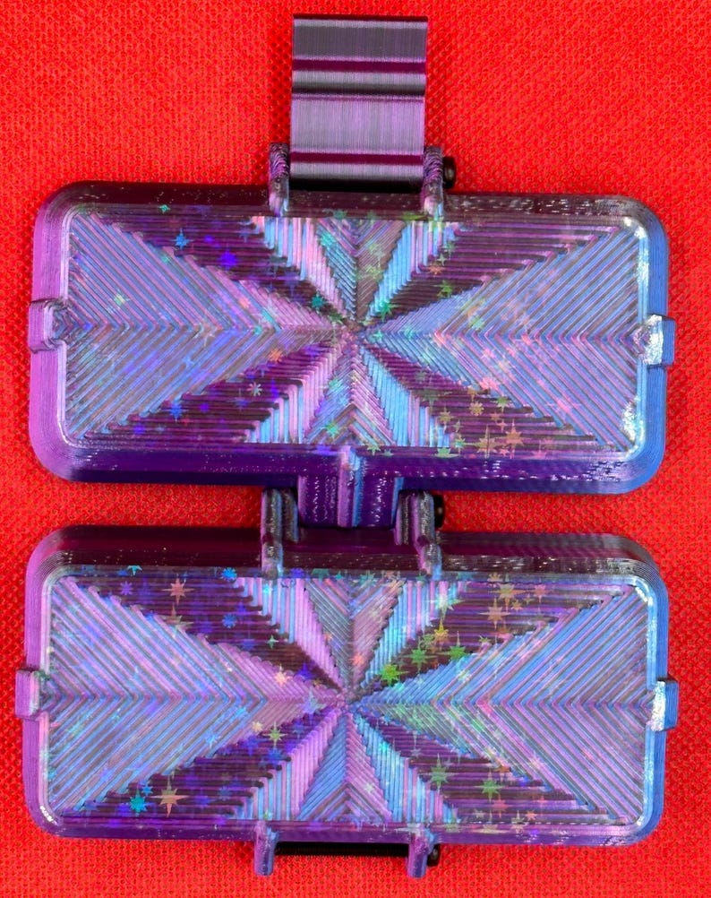 May include: A dual-section rectangular container featuring a deep purple frame and a holographic, star-patterned inlay. The surface displays a radiating geometric texture with iridescent blue and purple light reflections across the panels.