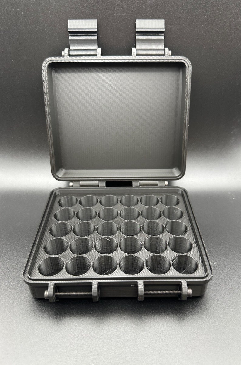 May include: A black, rectangular, open storage case featuring a grid of thirty circular compartments arranged in five rows of six. The case has a hinged lid with two top latches and a front locking mechanism, all constructed from a matte material.