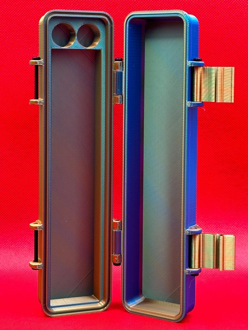 May include: A metallic blue and gold storage case with a hinged lid. The case has two small circular compartments on one side and a long, rectangular compartment on the other side.