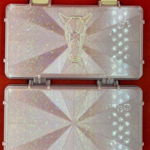 May include: Two iridescent white plastic boxes with a geometric pattern and a horse head design. The boxes are closed and have a hinge on the side.