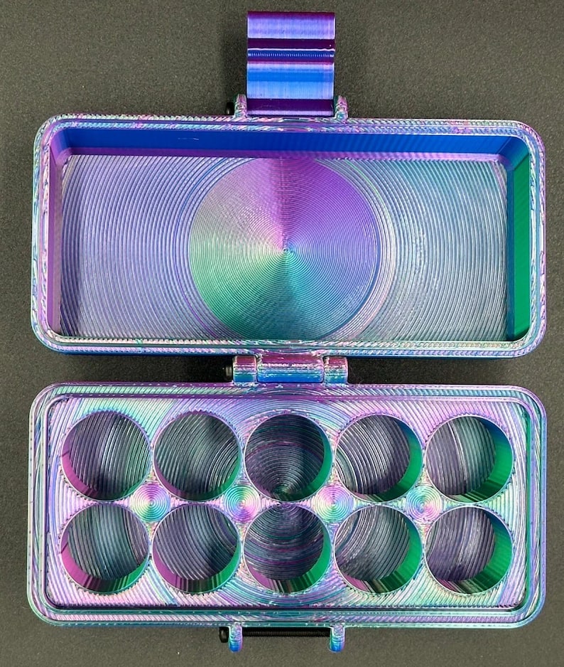 May include: A rectangular, hinged storage case with a vibrant, iridescent gradient finish shifting between blue, purple, and green. The top section is an open compartment, while the bottom section features ten circular cutouts for storage.