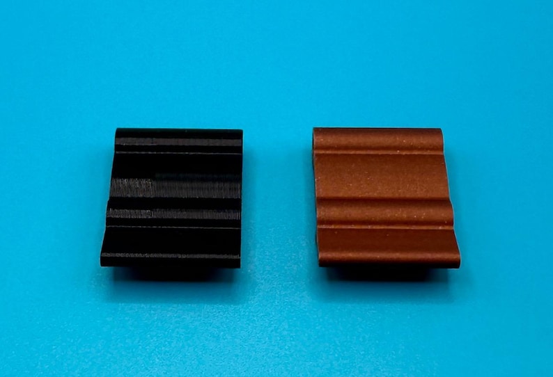 May include: Two rectangular clips with a wavy, grooved surface profile. One clip is solid black and the other is a metallic copper color. Both items feature a consistent, repeating horizontal ridge pattern across their top surfaces.