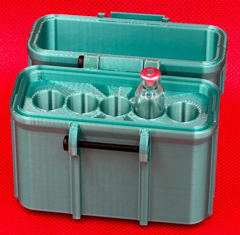 May include: A teal 3D-printed storage case with a hinged lid and a black metal latch mechanism. The interior features five circular slots designed for vials, with one clear glass vial containing a red cap inserted into the second slot.