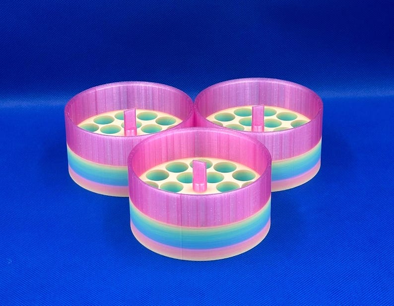May include: Three cylindrical organizers with a gradient finish transitioning from pink at the top to blue, green, and yellow at the base. Each container features a central vertical tab and a flat interior surface with multiple circular holes.
