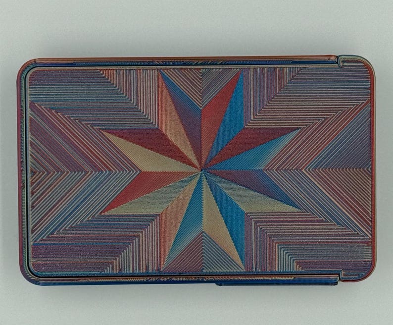 May include: Rectangular case with a starburst design. The case features a geometric pattern in shades of red, blue, and tan. The case has a metallic finish and a hinged lid.