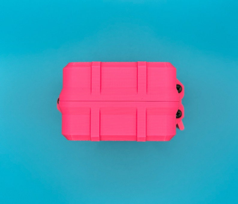 Puede incluir: Un estuche de almacenamiento rectangular de color rosa ne&oacute;n brillante con un exterior acanalado de estilo industrial. El estuche presenta dos tornillos negros visibles en el mecanismo de bisagra lateral y un cierre de pestillo seguro.