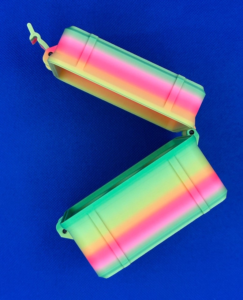 May include: A rectangular storage container with an open hinged lid, featuring a vibrant gradient color pattern that transitions through shades of pink, orange, yellow, and green. The box has a textured exterior with vertical ridges.