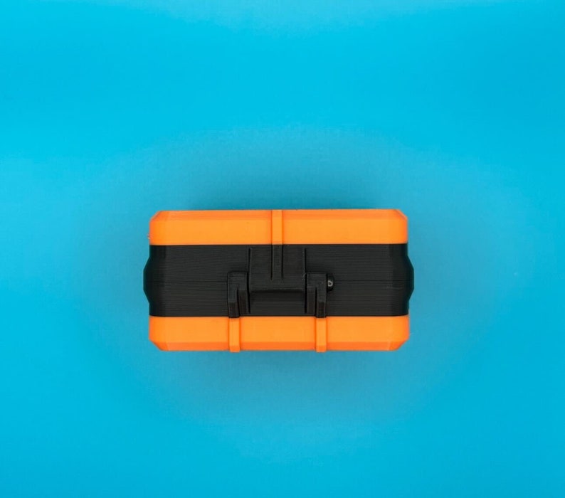 May include: A rectangular storage case featuring a vibrant orange top and bottom section separated by a wide black centre band. The case includes a central black handle mechanism integrated into the middle section, designed for secure closure.