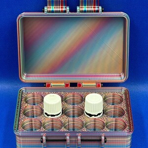 May include: A rectangular storage case with a hinged lid, featuring a multi-colored gradient pattern of horizontal and diagonal lines. The interior contains twelve circular compartments, with two white cylindrical caps visible inside.