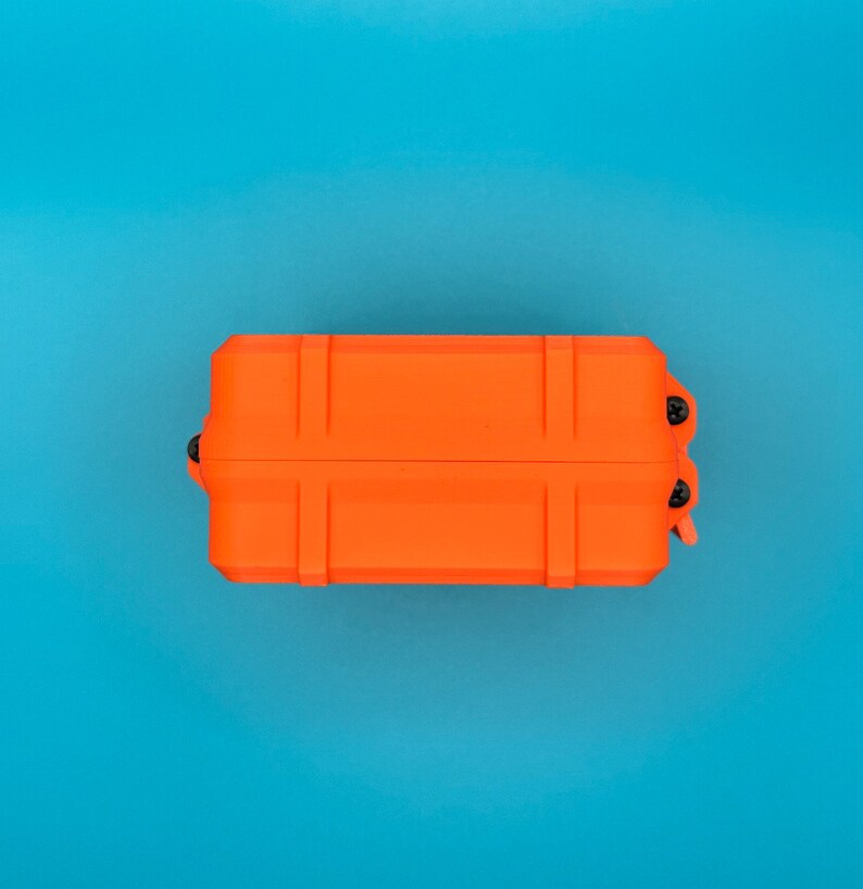 May include: A rectangular, bright orange protective storage case featuring a reinforced, ribbed exterior design. The case is secured with small black screws visible on the side hinges, providing a sturdy and compact enclosure for items.