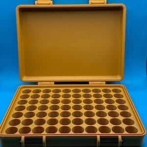 May include: A mustard yellow rectangular storage case with an open lid, featuring a grid of sixty circular compartments designed for organizing small items. The case has two front latches and two hinges, constructed with a textured finish.