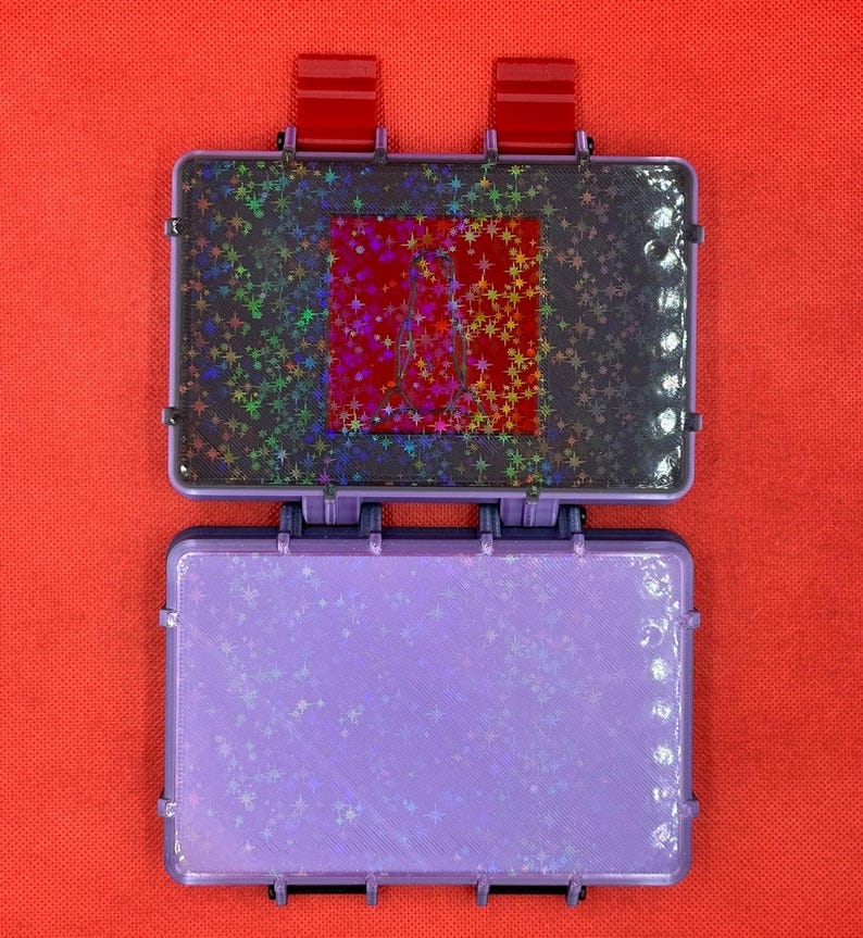May include: Open, purple, rectangular case with a holographic star pattern on the inside. The top section has a red square with a star pattern. The case is open, revealing the interior. The background is a solid red.