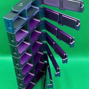 May include: A vertical storage organizer with multiple rectangular compartments featuring a shifting iridescent finish that transitions between deep purple and metallic green. The unit includes several hinged lids that swing outward.