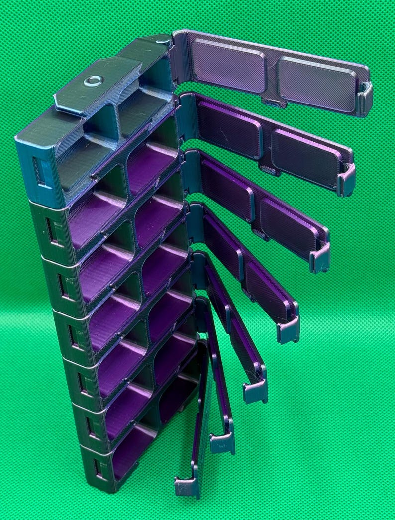 May include: A vertical storage organizer with multiple rectangular compartments featuring a shifting iridescent finish that transitions between deep purple and metallic green. The unit includes several hinged lids that swing outward.