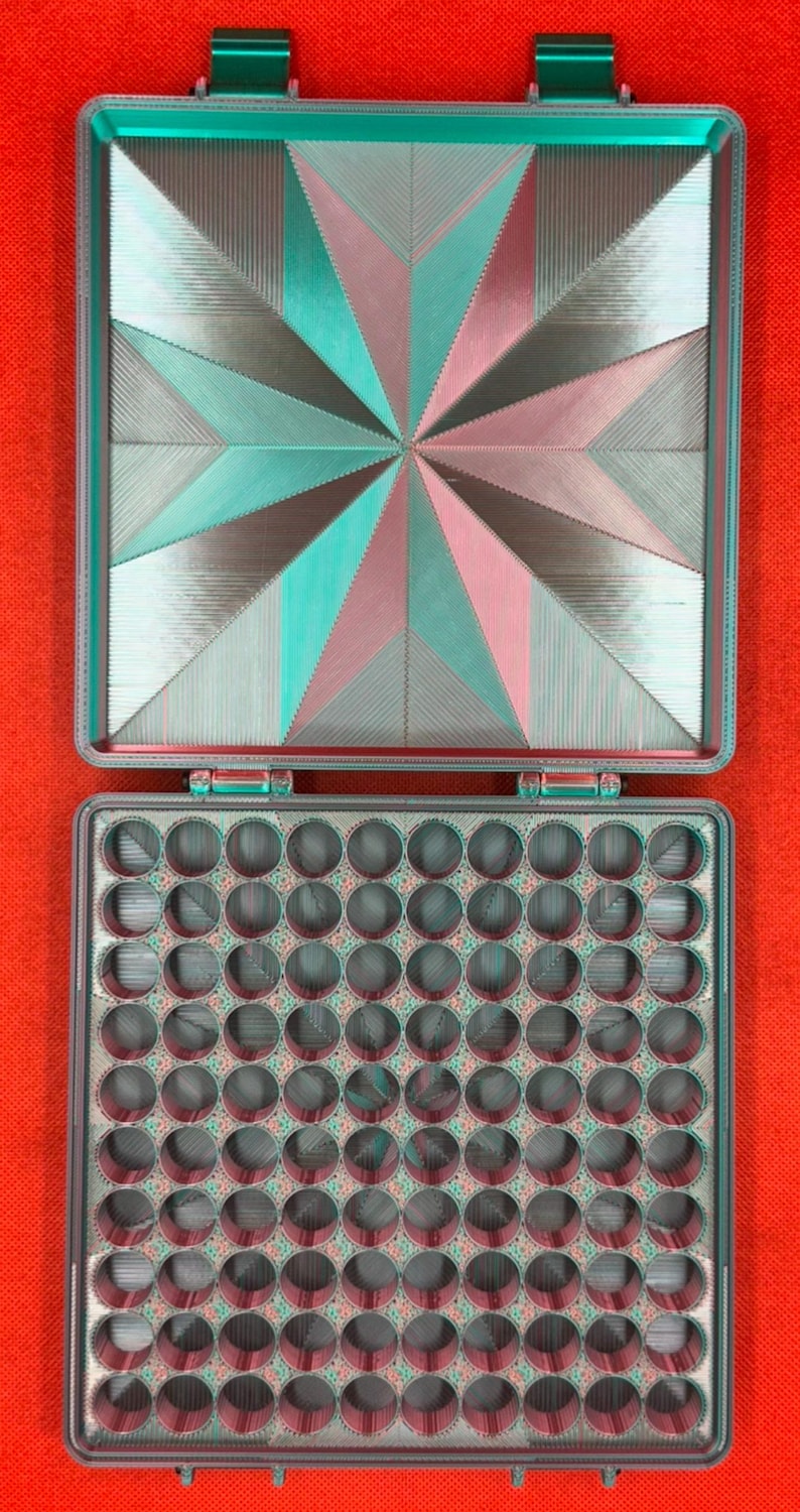 May include: A square, hinged storage case with a teal and pink geometric star pattern on the lid. The interior features a grid of one hundred circular compartments arranged in ten rows and ten columns, designed for organizing small items.