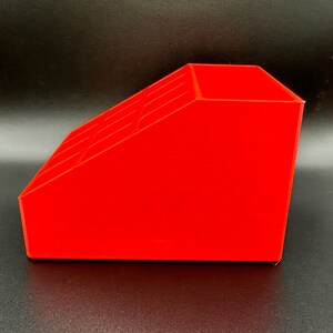May include: A bright red plastic organizer with multiple compartments. The organizer is angled and has a rectangular shape.