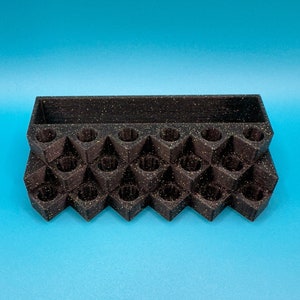 May include: A black, speckled, multi-tiered organizer stand featuring a rectangular storage compartment at the back and a series of twenty-one circular, recessed slots arranged in a grid pattern across the front stepped levels.