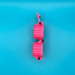May include: A bright pink, hinged, rectangular plastic case with a ribbed texture on the exterior. The case features three small black screws securing the hinges and closure mechanism, shown in a vertical orientation against a blue background.