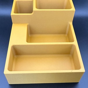 Op de afbeelding: Een gouden desktop organizer met vier vakken. De organizer heeft een rechthoekige vorm met een verhoogd gedeelte linksboven. De vakken zijn van verschillende groottes en diepten.