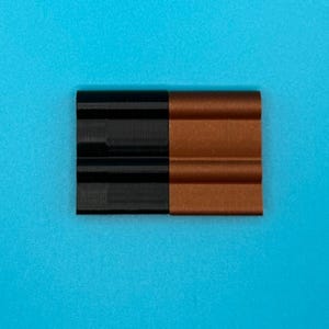 May include: A rectangular object composed of two side-by-side sections, one in solid black and the other in a metallic copper finish. Each section features a distinct horizontal ribbed or corrugated texture with three rounded ridges.