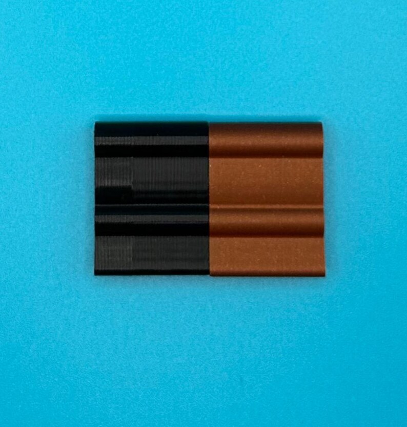 May include: A rectangular object composed of two side-by-side sections, one in solid black and the other in a metallic copper finish. Each section features a distinct horizontal ribbed or corrugated texture with three rounded ridges.