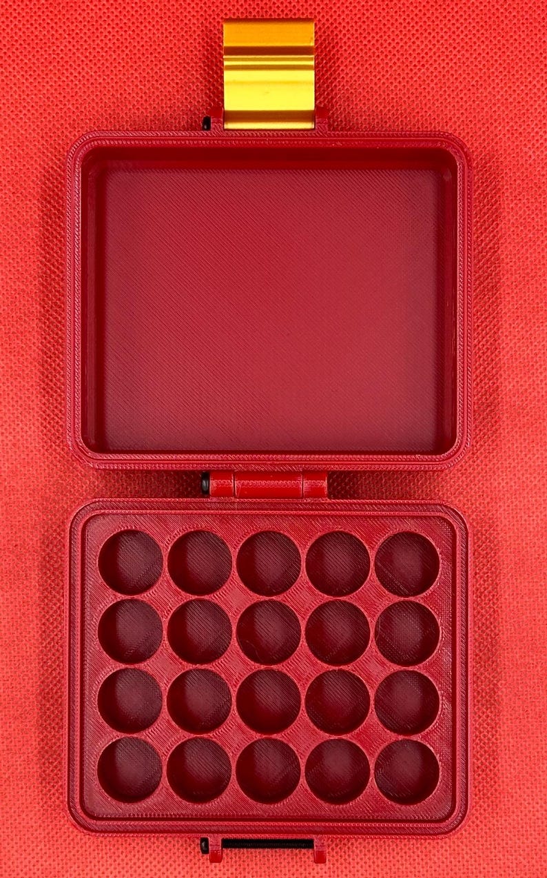 May include: A red rectangular storage case with a hinged lid and a gold-coloured metal latch. The interior of the base features a grid of twenty circular compartments arranged in four rows of five, while the lid interior is hollow.