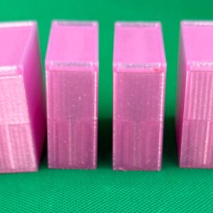 May include: Four rectangular, translucent pink plastic containers with lids. The two outer containers are wider than the two inner containers. Each container features a vertical ribbed texture on the sides and a smooth, flat top surface.