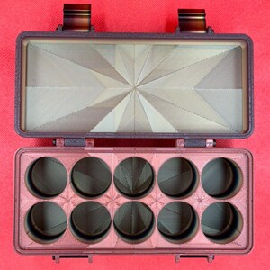 Puede incluir: Un estuche de almacenamiento rectangular de color marr&oacute;n oscuro impreso en 3D con tapa abatible. La base interior tiene diez compartimentos circulares en dos filas de cinco, y el interior de la tapa muestra un patr&oacute;n geom&eacute;trico de estrella.
