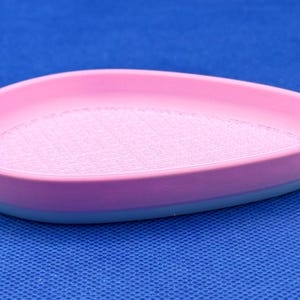May include: A pink and blue silicone dish with a textured surface. The dish is shaped like a teardrop and has a raised edge.