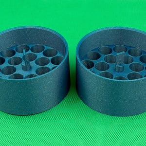 May include: Two dark blue, cylindrical containers with a textured finish. Each container features a flat base with multiple circular, hollow compartments arranged in a grid pattern and a small, vertical, rectangular tab in the center.