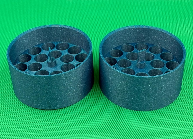 May include: Two dark blue, cylindrical containers with a textured finish. Each container features a flat base with multiple circular, hollow compartments arranged in a grid pattern and a small, vertical, rectangular tab in the center.