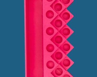 May include: A bright pink rectangular organizer tray featuring a long, deep storage compartment on the left side and a series of sixteen small, circular indentations arranged in a diamond-shaped grid pattern on the right side.