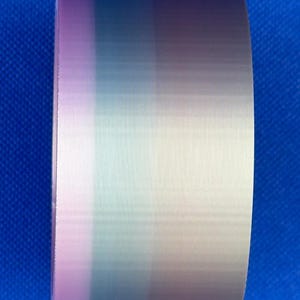May include: A roll of adhesive tape featuring a vertical gradient pattern that transitions through shades of soft pink, muted teal, light blue, and pale beige, displaying a smooth, semi-glossy finish with a fine, consistent texture.