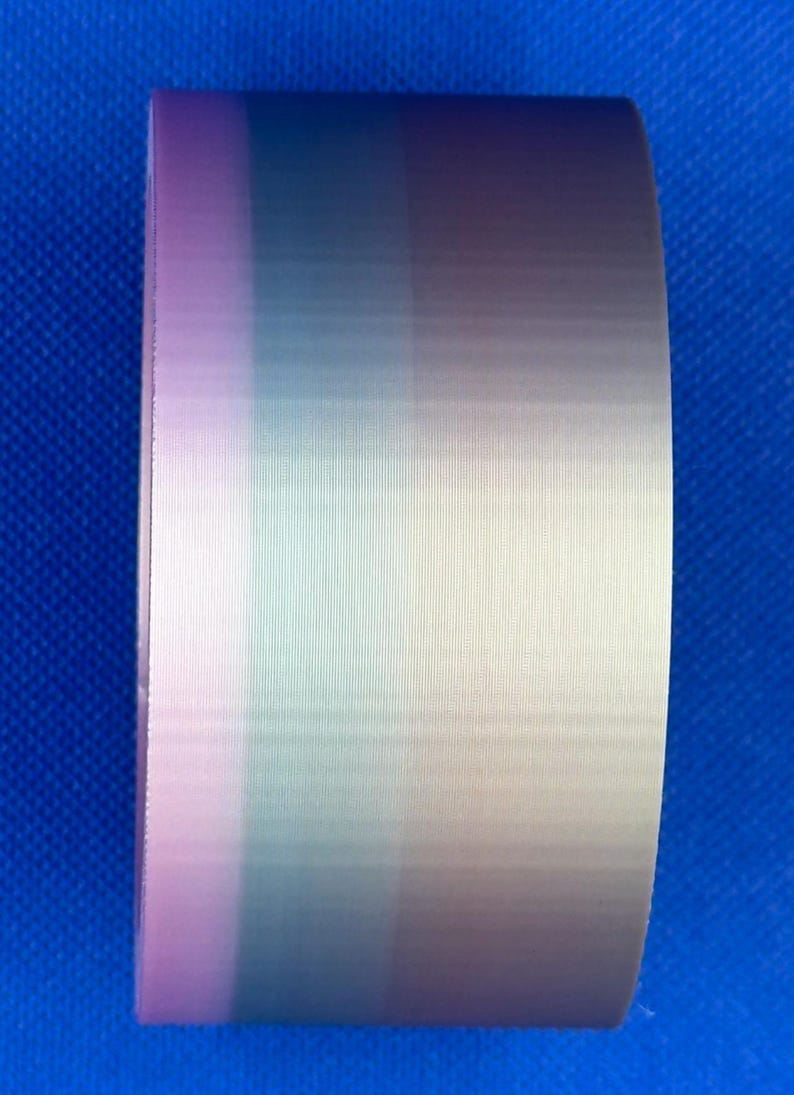 May include: A roll of adhesive tape featuring a vertical gradient pattern that transitions through shades of soft pink, muted teal, light blue, and pale beige, displaying a smooth, semi-glossy finish with a fine, consistent texture.