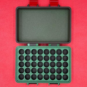May include: An open, green, rectangular case with a grid of circular holes, likely for storing small items. The case has a matching green interior and red latches. The background is a solid red.