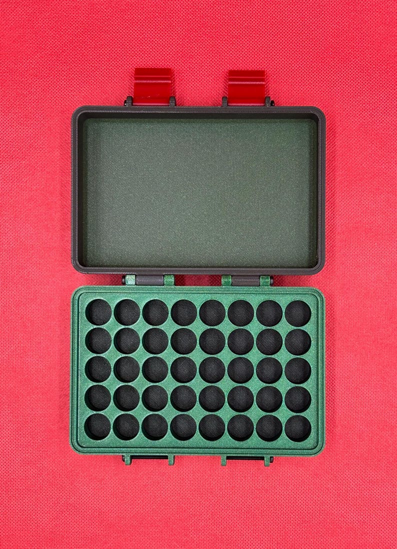 May include: An open, green, rectangular case with a grid of circular holes, likely for storing small items. The case has a matching green interior and red latches. The background is a solid red.