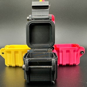 K&ouml;nnte beinhalten: Drei kleine, quadratische, 3D-gedruckte Aufbewahrungsbeh&auml;lter mit Klappdeckeln. Ein schwarzer Beh&auml;lter steht in der Mitte mit ge&ouml;ffnetem Deckel, w&auml;hrend ein gelber und ein pinker Beh&auml;lter jeweils dahinter auf beiden Seiten stehen.