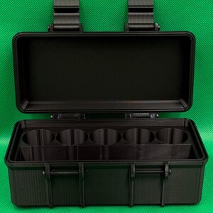 Puede incluir: Un estuche de almacenamiento rectangular negro con tapa abatible y dos cierres superiores. El interior cuenta con cinco compartimentos cil&iacute;ndricos circulares dispuestos en fila y un espacio rectangular frente a ellos.