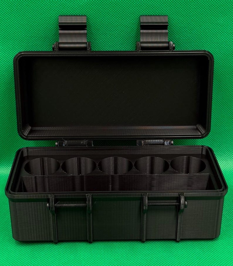 Puede incluir: Un estuche de almacenamiento rectangular negro con tapa abatible y dos cierres superiores. El interior cuenta con cinco compartimentos cil&iacute;ndricos circulares dispuestos en fila y un espacio rectangular frente a ellos.