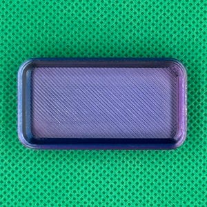 May include: A rectangular, 3D-printed tray with a textured, diagonal pattern in shades of purple and blue. The tray has rounded corners and a dark blue border, set against a green background.